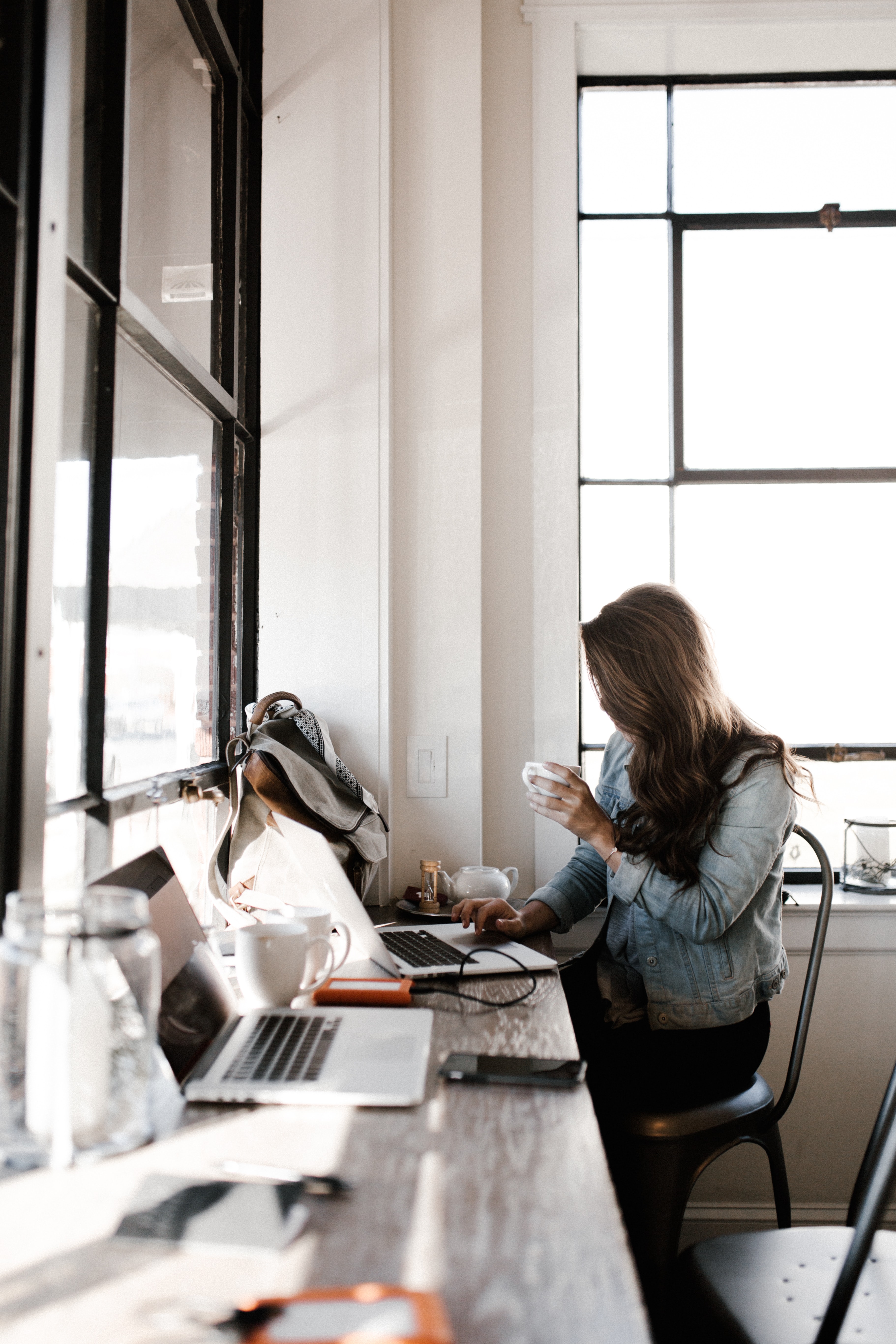 A lady sitting and working with her laptop and holding a cup of coffee with the other hand
